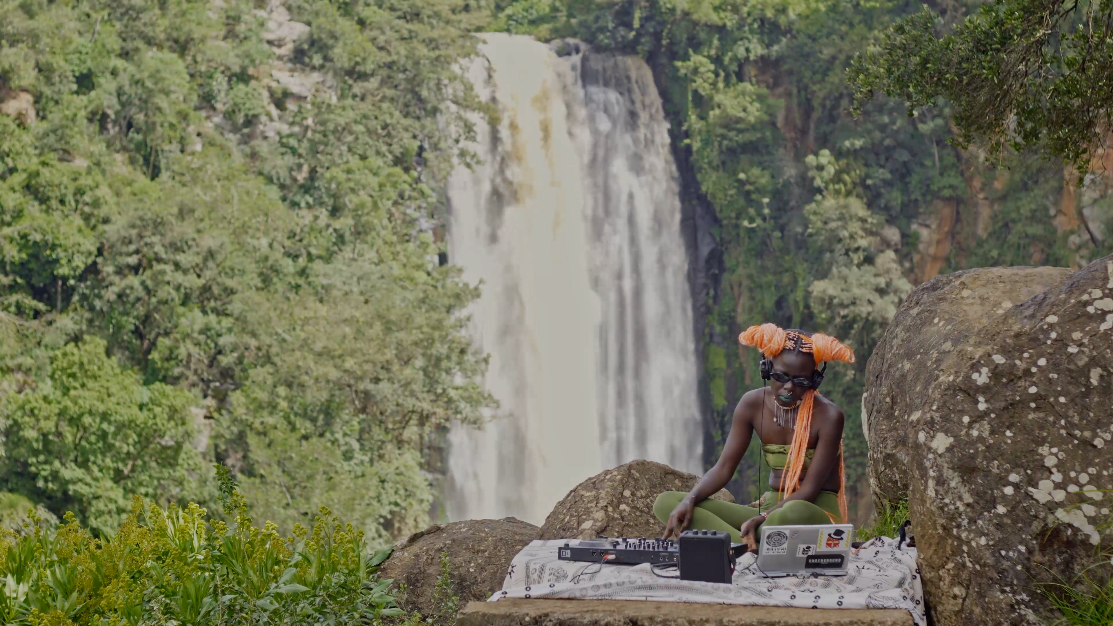 «Warme Fronten» ist ein Kunst-Werk des Künstlers Kent Chan. Makossiri tritt in «Warme Fronten» vor einem tropischen Wasser-Fall auf. Makossiri ist eine Musikerin und DJ.
